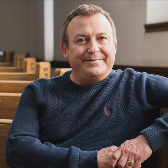 Peter, middle-aged white man, sitting in an empty church, looking at camera.